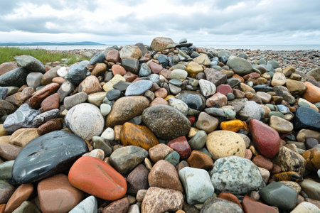 Various multicolored stones form a natural mound on the beach, with a cloudy sky prominently overhead.の写真素材