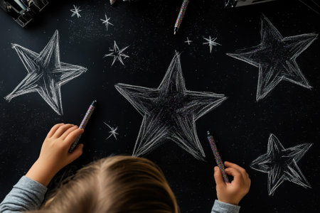 A child draws stars with chalk on black paper, showing creativity and artistic expression during art time.の写真素材
