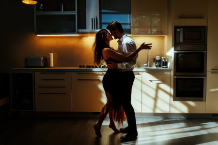 A couple shares a passionate dance in a stylish kitchen, bathed in warm, glowing light from windows.の写真素材