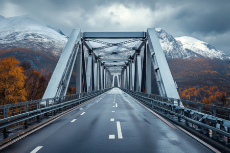 Modern bridge stretches over a smooth road with mountains and colorful autumn trees in the background.の写真素材