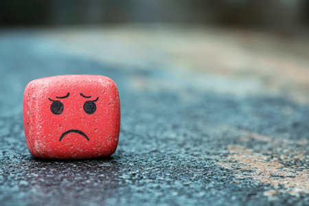 A small red stone with sad facial expression rests on a rough outdoor surface, conveying loneliness.の写真素材