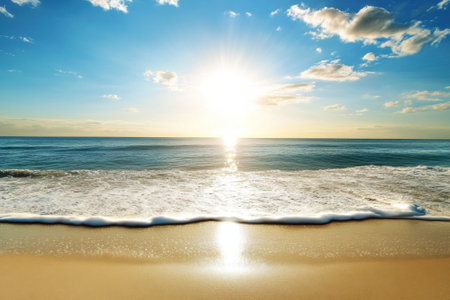 Vivid colors of the rising sun reflect on the ocean while gentle waves kiss the sandy shore.の写真素材