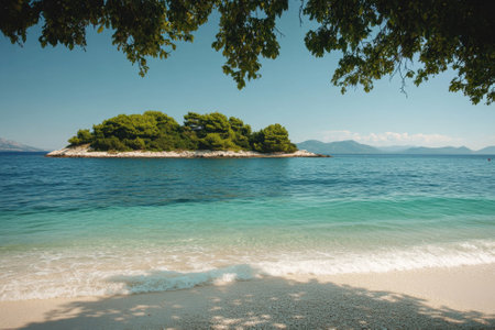 Gentle waves lap against the shore as sunlight illuminates a tranquil beach with an island nearby.の写真素材