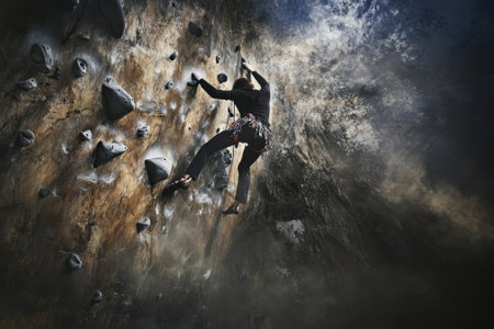 A determined climber navigates challenging holds on a textured wall in an indoor climbing gym with dim lighting.の写真素材
