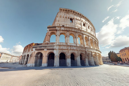 Visitors admire the grandeur of the Colosseum in Rome during a clear day with fluffy clouds.の写真素材