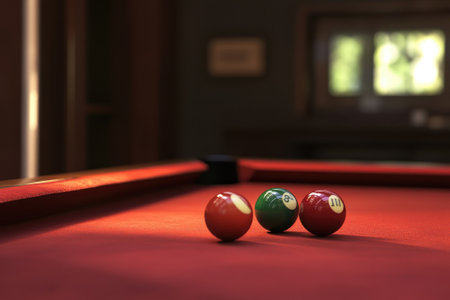 Three billiard balls, one green, one red, and one striped, sit on a red table in a cozy game room.の写真素材