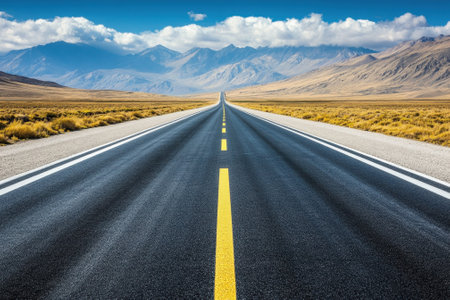 A long road stretches through golden plains toward majestic mountains under a bright blue sky.の写真素材