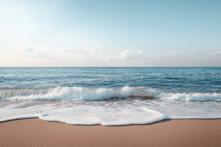 Waves break softly on the shore, creating frothy patterns on the golden sand at sunset.の写真素材