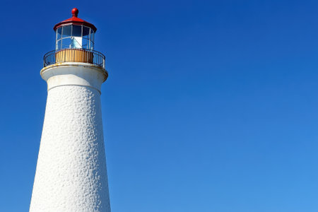 A tall white lighthouse with a red top overlooks the endless blue sky, embodying maritime heritage and guidance.の写真素材