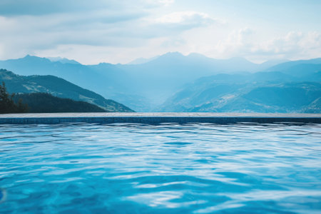 Calm waters of an infinity pool reflect stunning mountains under a clear sky in the afternoon.の写真素材