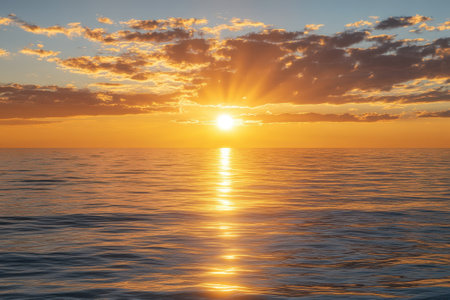A stunning sunset casts golden rays across calm ocean waters, creating a serene atmosphere at twilight.の写真素材
