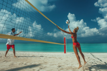 A woman serves a volleyball during a fun match on the beach with a man at the net amidst clear blue skies.の写真素材