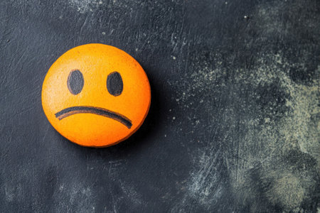 A round orange stone displays a sad face design, placed against a dark textured surface highlighting its color.の写真素材