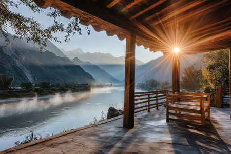 Early morning light illuminates a peaceful river as mist rises, framed by mountains and a wooden porch.の写真素材