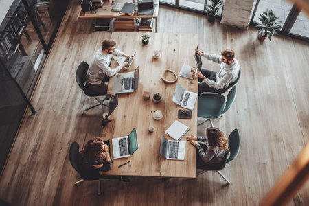 Four professionals engaging in a project discussion while working on laptops in a stylish office environment.の写真素材