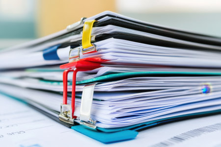 Multiple binders filled with documents are stacked neatly on a table in a bright office environment.の写真素材