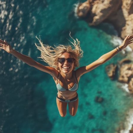 A smiling woman in a bikini leaps into crystal-clear coastal waters, enjoying her summer adventure.の写真素材