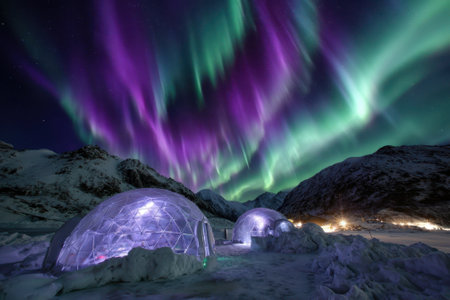 Colorful auroras illuminate the sky above igloos in a remote, wintry location during the night.の写真素材