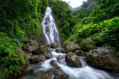 A beautiful waterfall flows over rocks in a dense forest, surrounded by vibrant greenery during daylight.の写真素材
