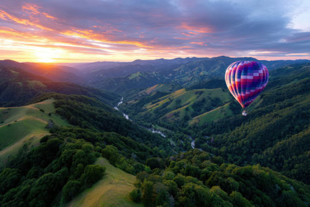 A vibrant hot air balloon soars above lush green hills as the sun rises, illuminating the landscape with warm colors.の写真素材
