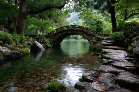 A stunning stone bridge spans calm waters, encircled by lush greenery and vibrant flowers, evoking tranquility.の写真素材