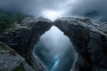 A magnificent stone arch overlooks a foggy valley with a serene river, showing nature's grandeur at dusk.の写真素材