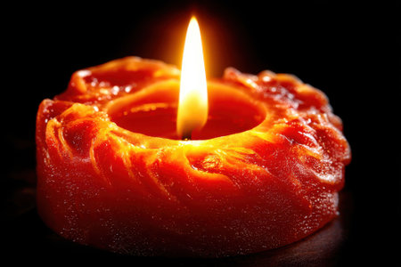A bright flame dances on a vibrant orange candle, adding warmth and tranquility to a dimly lit space.の写真素材