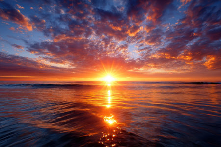 Vibrant colors of sunset fill the sky as sun dips below the horizon, casting a warm glow on ocean waters.の写真素材