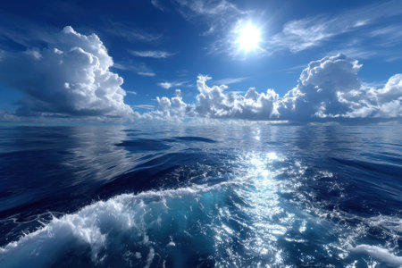Bright sunlight reflects on calm ocean waters, creating a serene atmosphere with fluffy clouds overhead.の写真素材