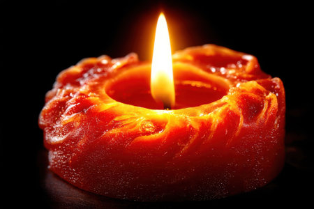 A bright flame dances on a vibrant orange candle, adding warmth and tranquility to a dimly lit space.の写真素材