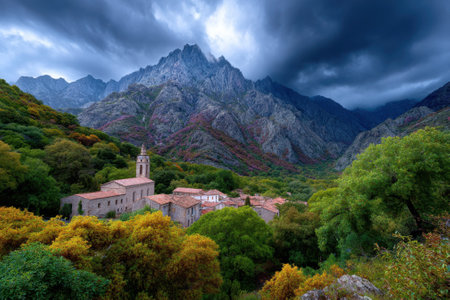 A tranquil village nestled in mountains showcases vibrant autumn colors under a moody sky.の写真素材