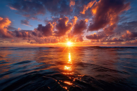 The sun sets brilliantly over the calm ocean, casting warm hues across the sky and water.の写真素材
