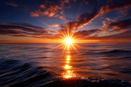 Golden sunlight glistens on the ocean waves as the sun sets on the horizon, painting the sky in warm colors.の写真素材