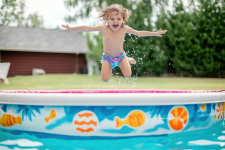 A young child with curly hair leaps into a colorful inflatable pool filled with water.の写真素材