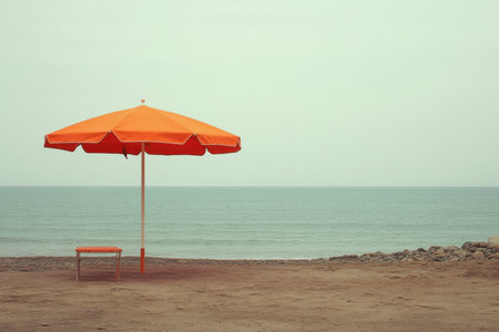 A vibrant orange umbrella is set on a deserted sandy beach overlooking the calm sea under an overcast sky.の写真素材