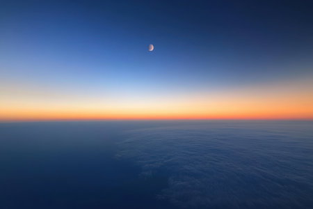 A crescent moon hangs in the twilight sky above the tranquil ocean, creating a peaceful atmosphere at dusk.の写真素材