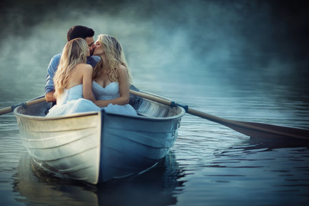 Three individuals share a romantic kiss in a small boat on a calm lake at dusk.の写真素材