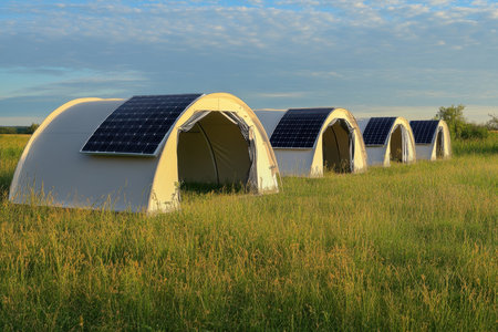 Four eco-friendly tents with solar panels are arranged in a lush green field under a clear blue sky.の写真素材