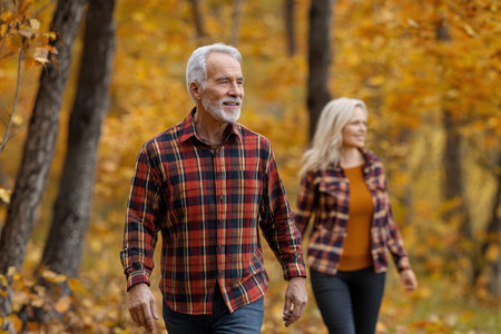 Two adults stroll through a forest, adorned with vibrant autumn leaves, enjoying a peaceful outdoor moment.の写真素材