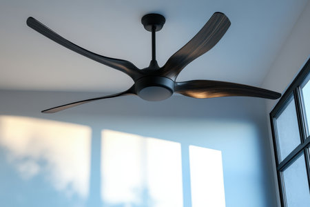 A sleek ceiling fan hangs from the ceiling, surrounded by soft natural light streaming through windows.の写真素材