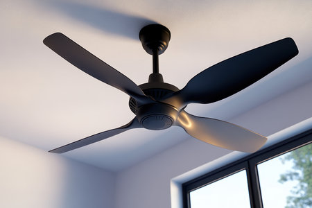 A sleek black ceiling fan spins gently in a bright room with large windows, providing a cool atmosphere.の写真素材