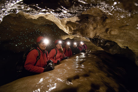 A group of four explorers dressed in red jackets navigate a cave, using headlamps to light the dark passage.の写真素材