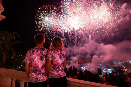 Couple stands together on a balcony, watching colorful fireworks light up the sky in a vibrant display.の写真素材