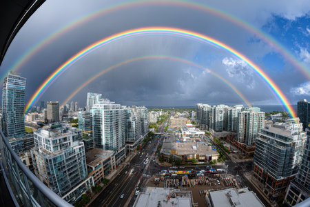 Double rainbow arches over a city skyline with tall buildings and roadsの写真素材