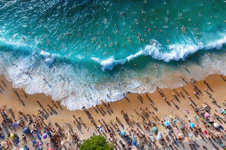 Numerous beachgoers relax on the sand and swim in the ocean under bright sunlight.の写真素材