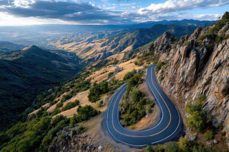A winding mountain road snakes through a valley below a cloudy sunset skyの写真素材