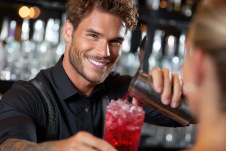 Smiling bartender mixes vibrant cocktail for customer in a bustling bar during the evening.の素材
