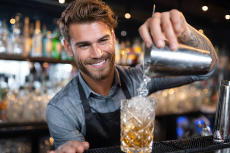 A skilled bartender mixes a cocktail, showing a friendly smile in a bustling bar as night falls.の素材