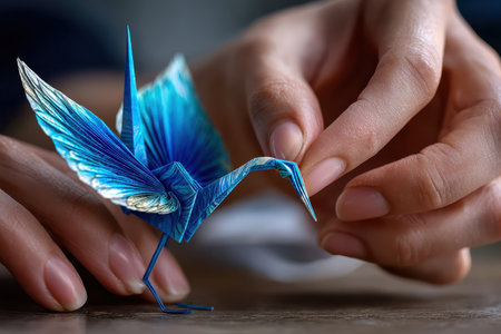 A hand shapes a blue origami crane with precision, showing skilled craftsmanship and attention to detail.の写真素材