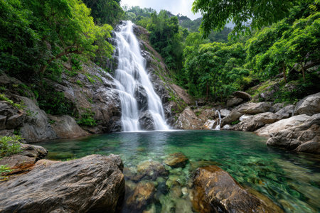 Waterfall cascading into a clear emerald pool in a lush green forestの写真素材